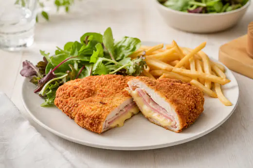 Un cordon bleu coupé en deux, panure dorée, jambon et fromage fondu qui coule, servi avec une salade et des frites